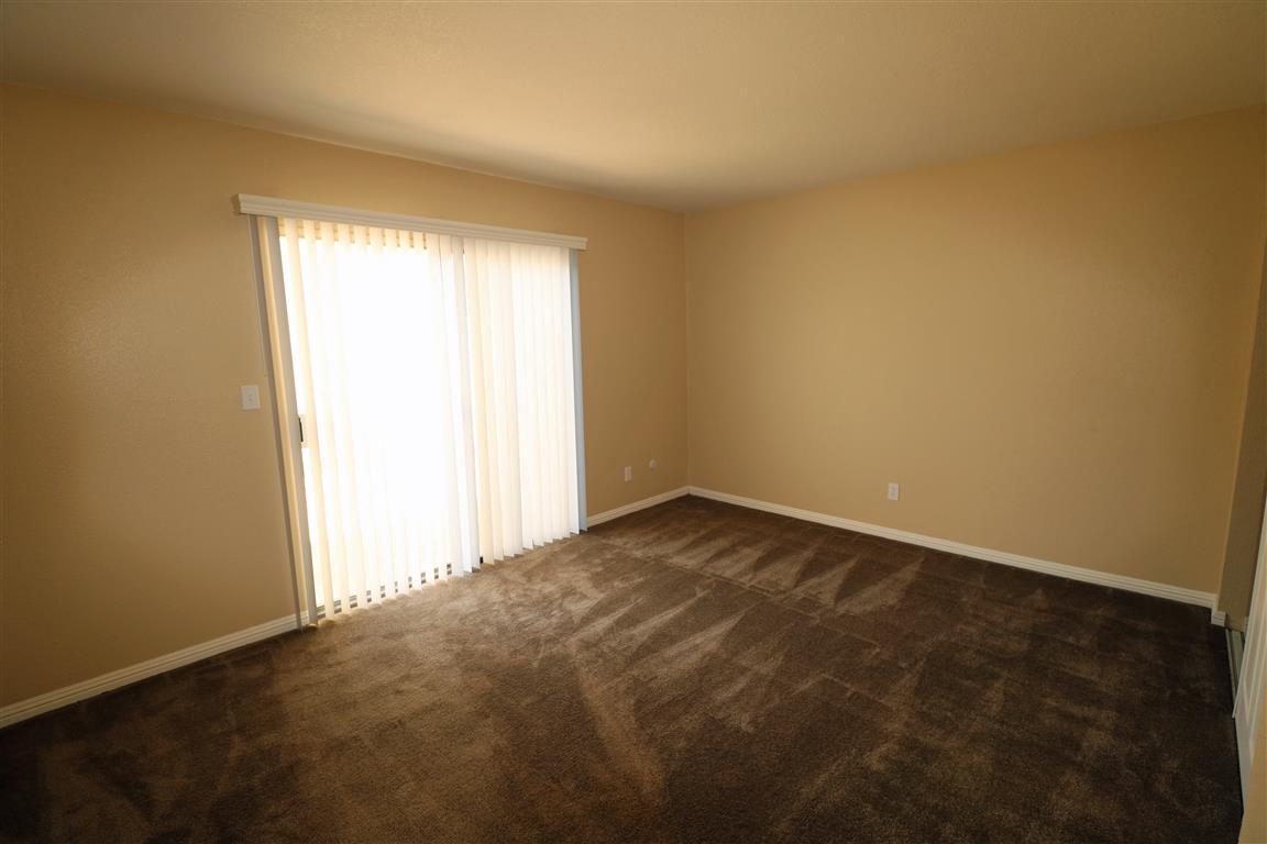 A room with brown carpet and a window with white curtains.